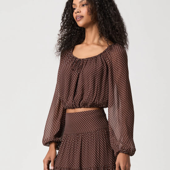 Woman wearing spotty brown and cream blouse on white background side view