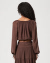 A woman shown from the back wearing a brown off-the-shoulder long-sleeve crop top and matching pleated skirt, both featuring a small white polka dot pattern, against a light gray studio background.