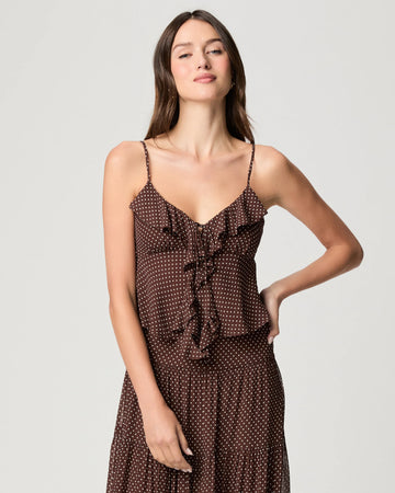 A woman modeling a brown spaghetti-strap dress with a white polka dot pattern and a ruffled tie detail at the bust, set against a plain light gray studio background.