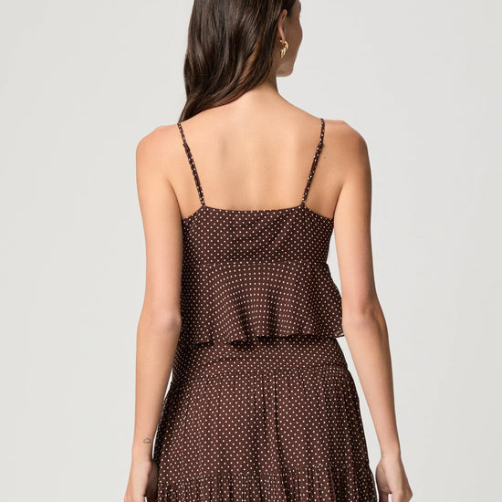 A woman shown from the back wearing a dark brown spaghetti-strap dress with a small white polka dot pattern, set against a plain light gray studio background.