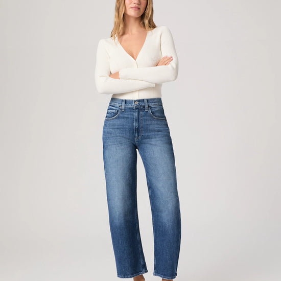 Woman wearing a white sweater and blue jeans on a plain background