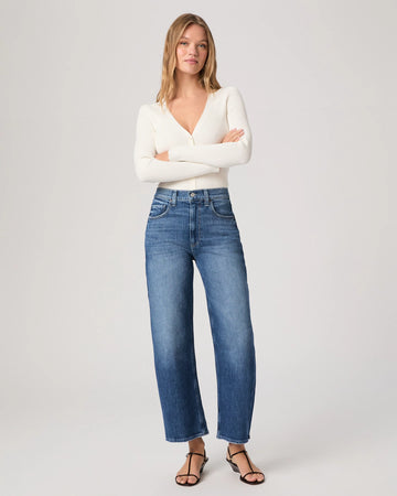 Woman wearing a white sweater and blue jeans on a plain background
