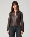 A woman modeling a dark brown leather jacket with a split collar and front zipper, paired with dark gray jeans, against a light gray studio background.