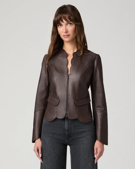 A woman modeling a dark brown leather jacket with a split collar and front zipper, paired with dark gray jeans, against a light gray studio background.