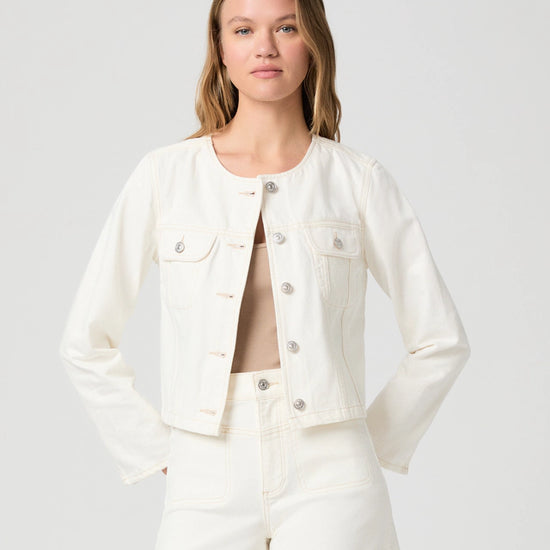 Woman wearing a cream Paige denim jacket and shorts on a plain background