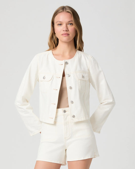 Woman wearing a cream Paige denim jacket and shorts on a plain background