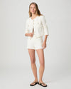 Woman wearing a cream Paige denim jacket and shorts on a plain background, full body shot 
