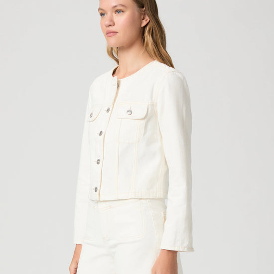 Woman wearing a cream Paige denim jacket and shorts on a plain background side view