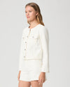 Woman wearing a cream Paige denim jacket and shorts on a plain background side view