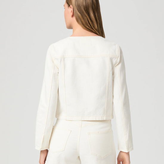 Woman wearing a cream Paige denim jacket and shorts on a plain background rear view