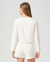 Woman wearing a cream Paige denim jacket and shorts on a plain background rear view
