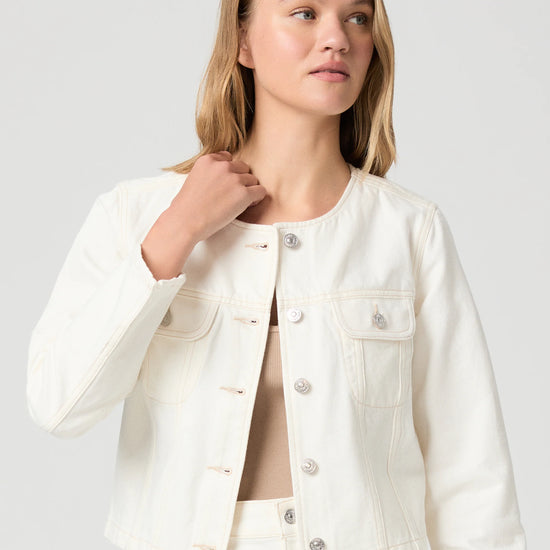 Woman wearing a cream Paige denim jacket and shorts on a plain background close up