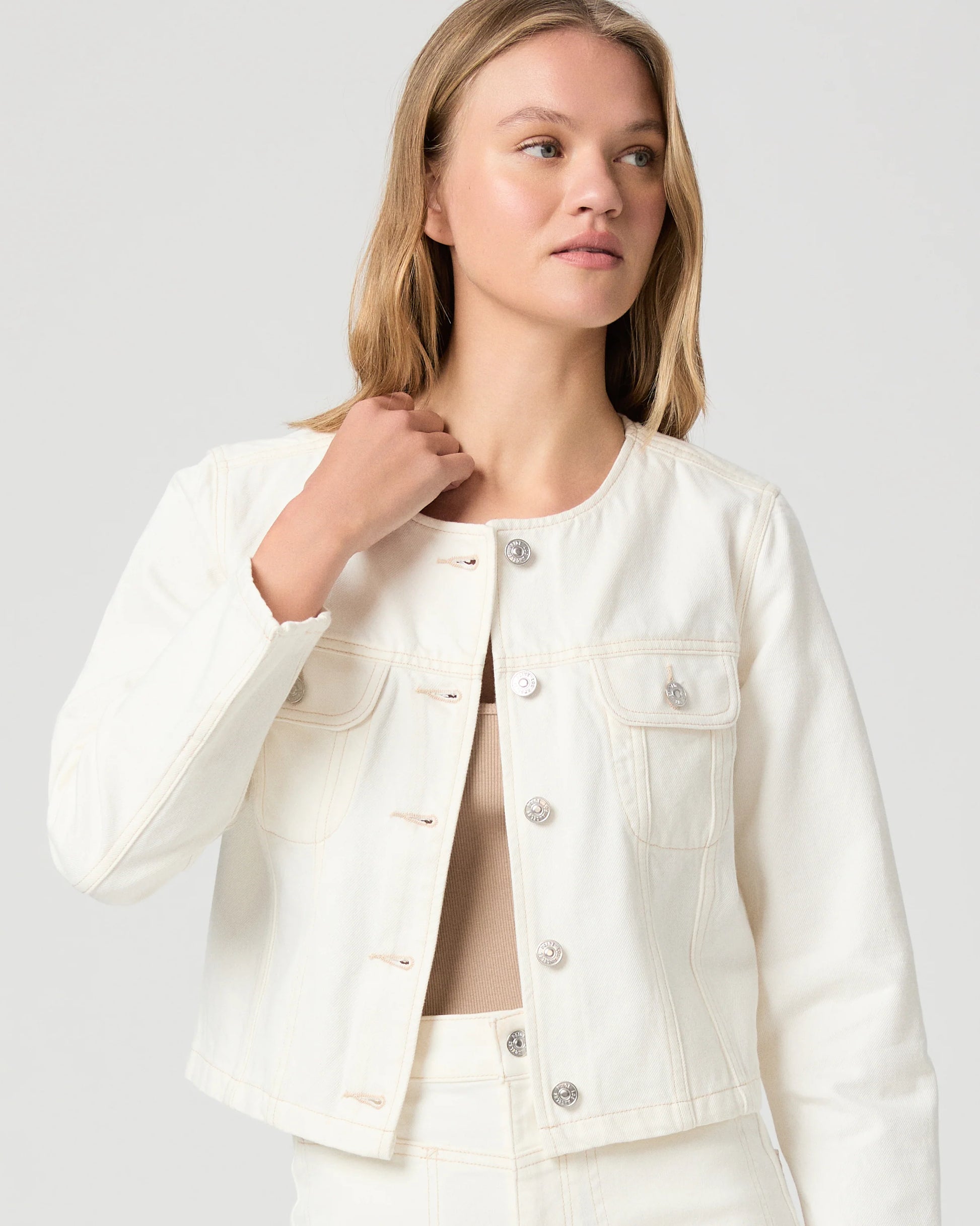 Woman wearing a cream Paige denim jacket and shorts on a plain background close up