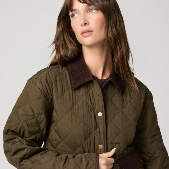 A woman wearing an olive green diamond-quilted jacket with a dark brown corduroy collar and brown button details, photographed against a neutral light gray background.