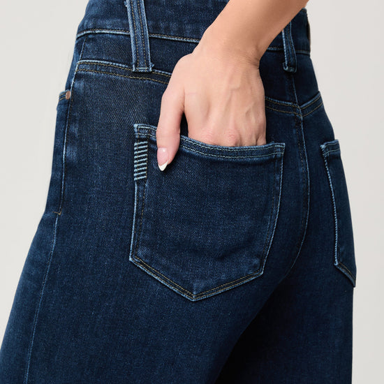 Person wearing dark blue jeans with a hand in the pocket on a light gray background