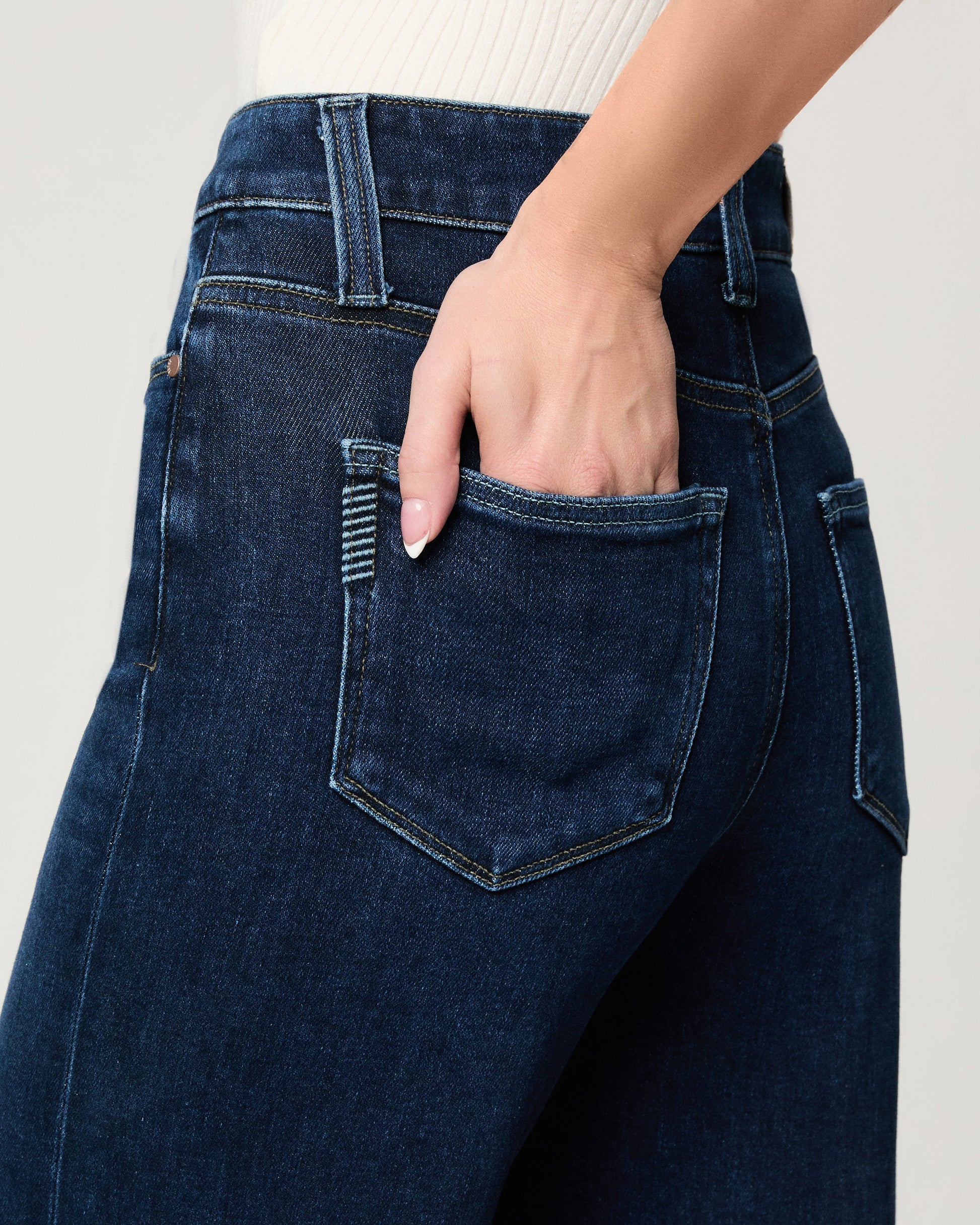 Person wearing dark blue jeans with a hand in the pocket on a light gray background