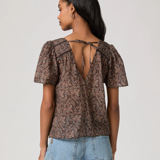 woman wearing a brown paisley blouse and jeans rear view