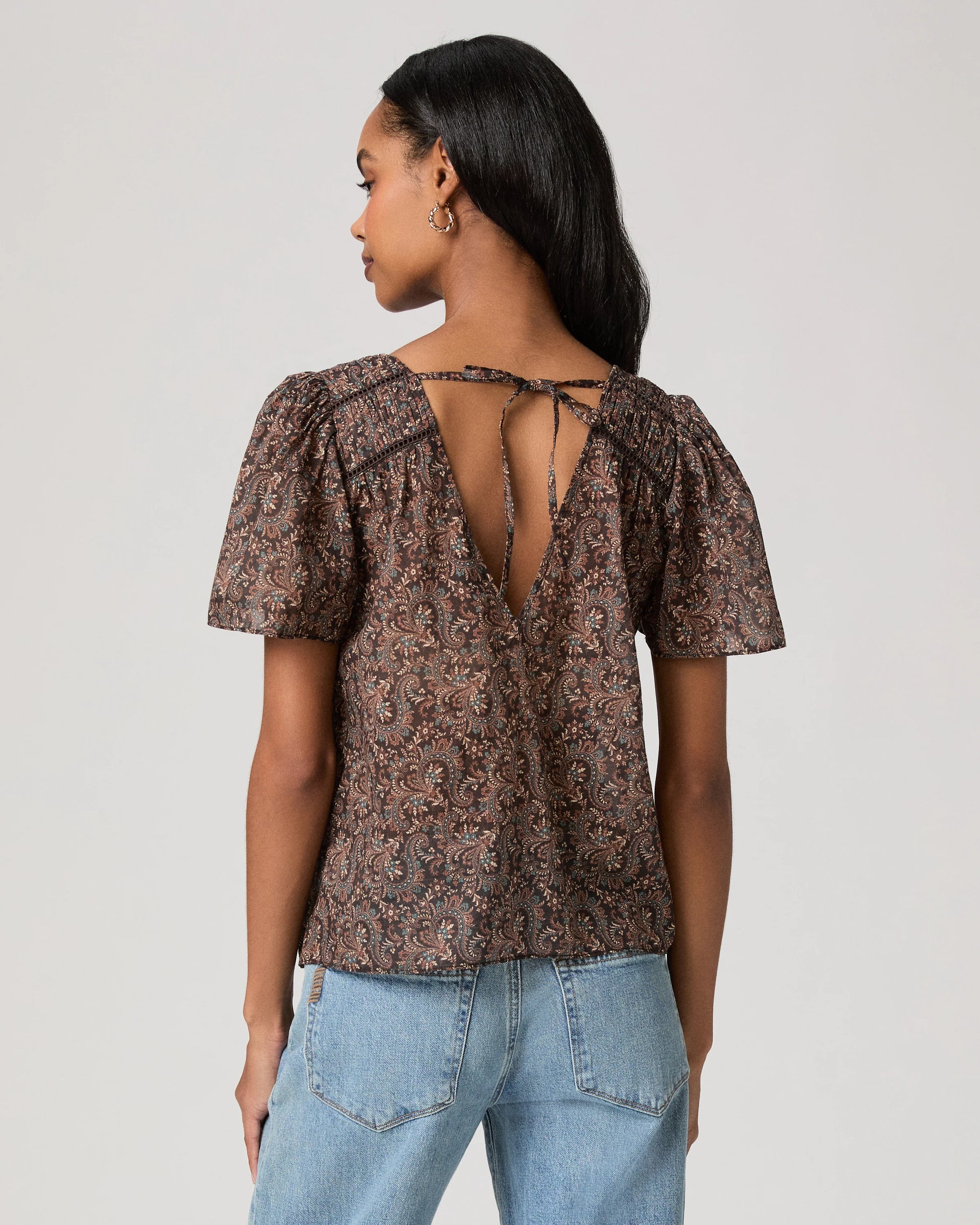 woman wearing a brown paisley blouse and jeans rear view