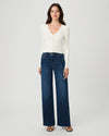 A woman modeling a white long-sleeve V-neck knit top and dark blue wide-leg jeans against a light gray studio background.
