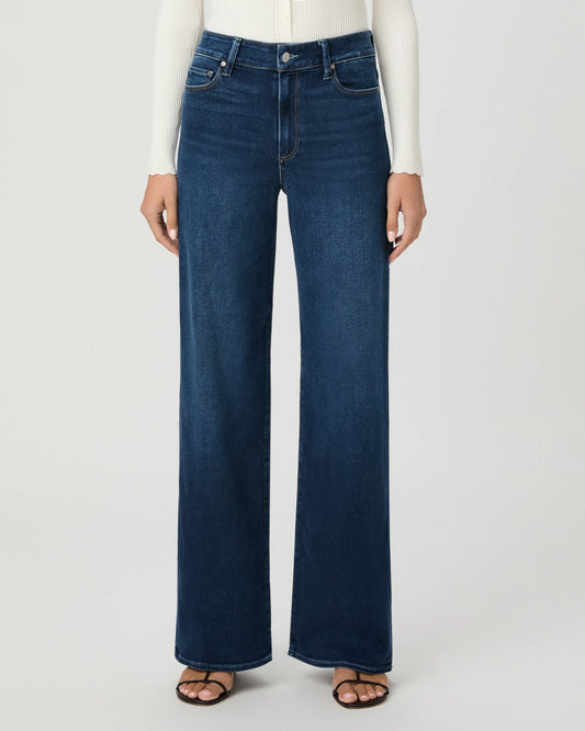 A model wearing dark blue wide-leg denim jeans, a white ribbed long-sleeve top, and brown sandals, shown from the waist down against a light gray studio background.