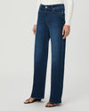 A model wearing dark blue wide-leg jeans, a white ribbed long-sleeve top, and brown flat sandals, shown from the waist down against a light gray studio background.