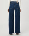 Back view of a model wearing dark blue wide-leg denim jeans with a white long-sleeve top, shown against a light gray studio background.