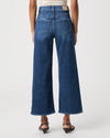 A model shown from the back wearing a pair of wide-leg cropped blue denim jeans, paired with a striped top and dark brown heeled sandals, against a light gray studio background.