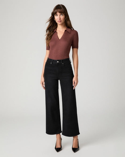A woman modeling a short-sleeve ribbed knit polo shirt in a muted reddish-brown color paired with black wide-leg cropped jeans and black pointed heels, shot against a light gray studio background.