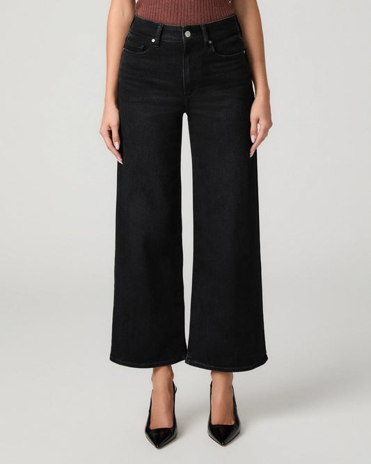 A model wearing a pair of black wide-leg cropped jeans with a ribbed top and black pointed-toe heels, photographed against a light gray studio background.
