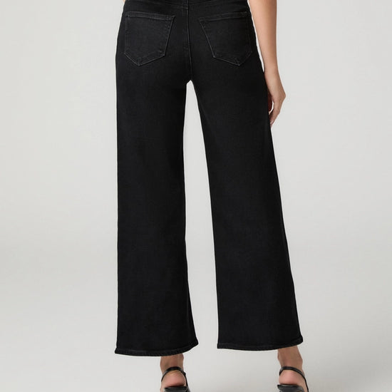 Black wide-leg cropped jeans shown from the back on a model, paired with black high-heeled sandals against a light gray studio background.
