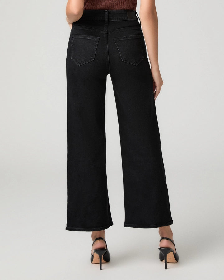 Black wide-leg cropped jeans shown from the back on a model, paired with black high-heeled sandals against a light gray studio background.