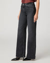 A model wearing a pair of dark gray wide-leg denim jeans, paired with a burgundy top and black pointed-toe heels, shown from the waist down on a light gray studio background.