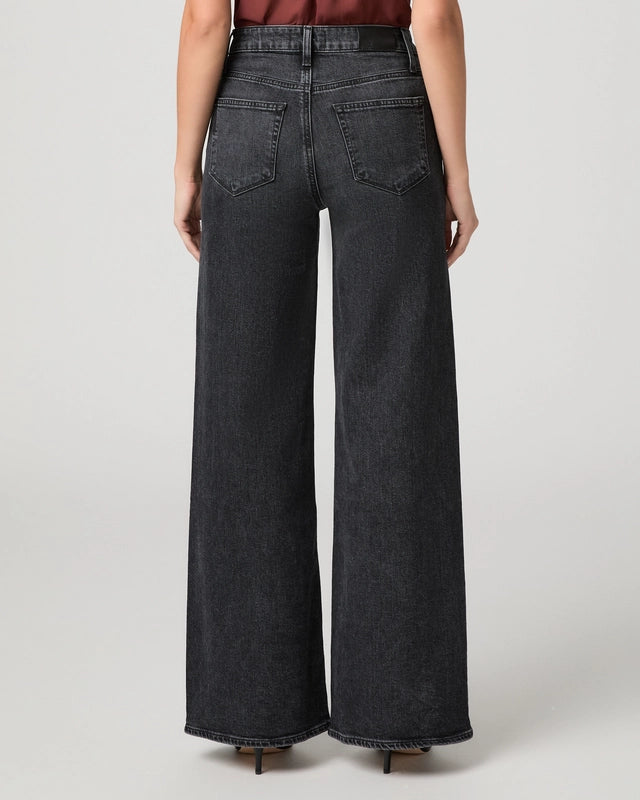 Rear view of a model wearing dark gray wide-leg denim jeans with a faded wash, paired with a dark red top and black heels, against a light gray studio background.