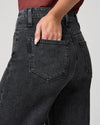 Close-up back view of a person wearing dark charcoal gray washed jeans, with one hand tucked into the back pocket, against a light gray studio background.