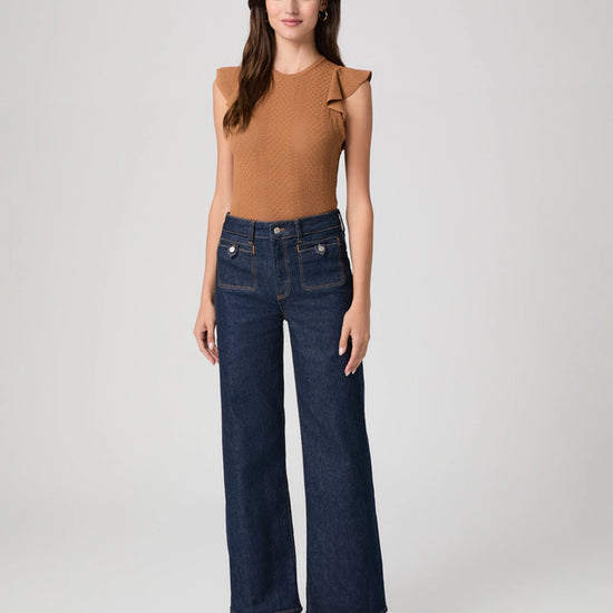 Woman wearing a brown top and dark blue jeans on a white background