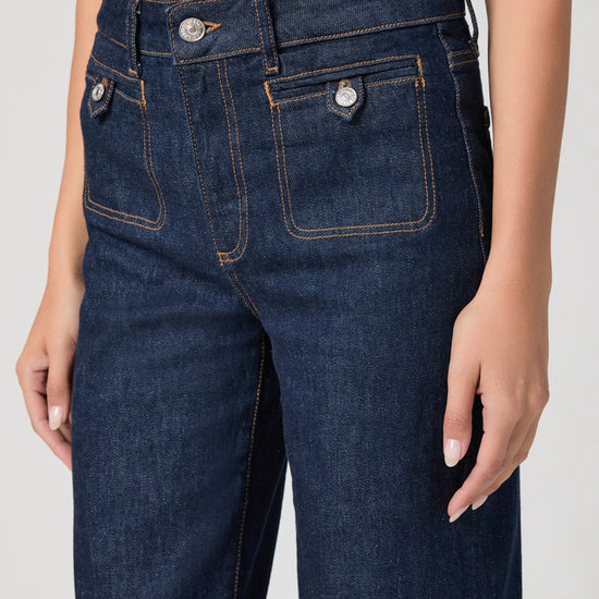 Dark blue jeans worn by a person on a plain background