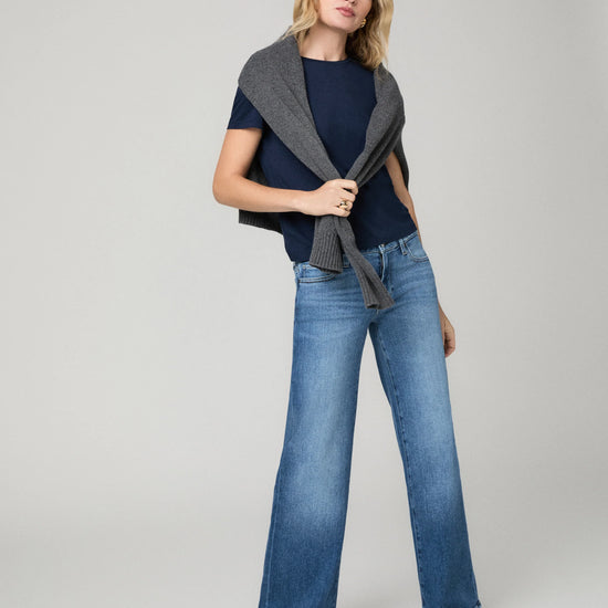 Model wearing blue jeans with navy top and grey jumper on a grey background