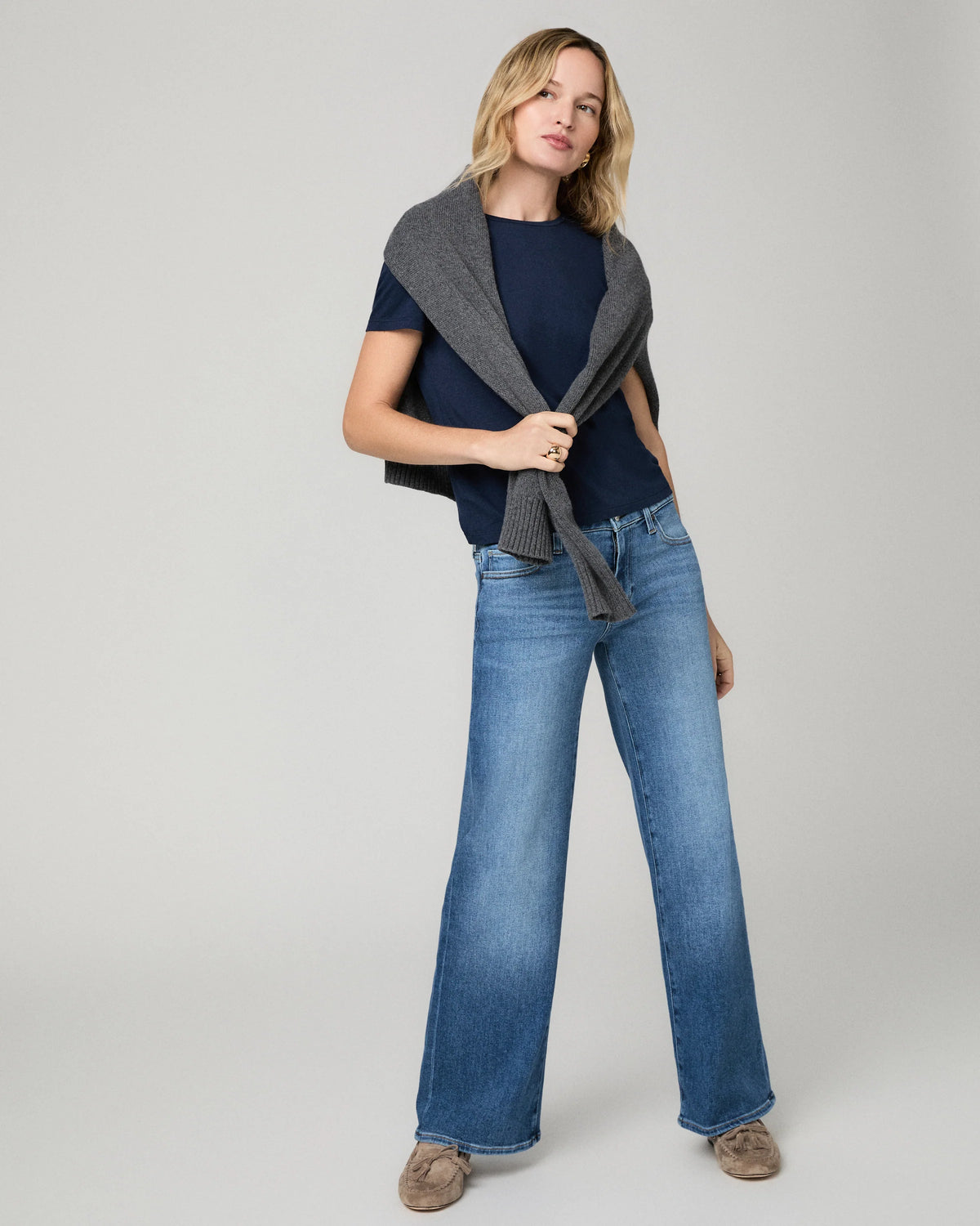 Model wearing blue jeans with navy top and grey jumper on a grey background