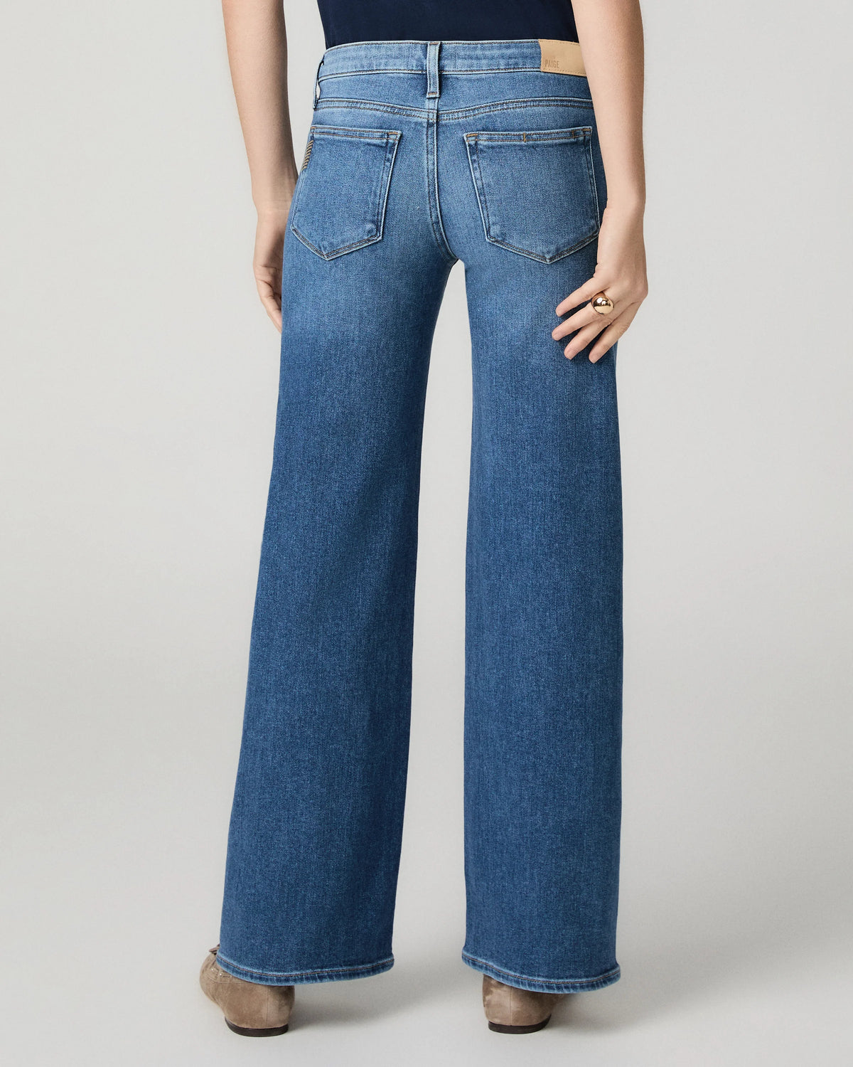 Model wearing blue jeans on a grey background rear view