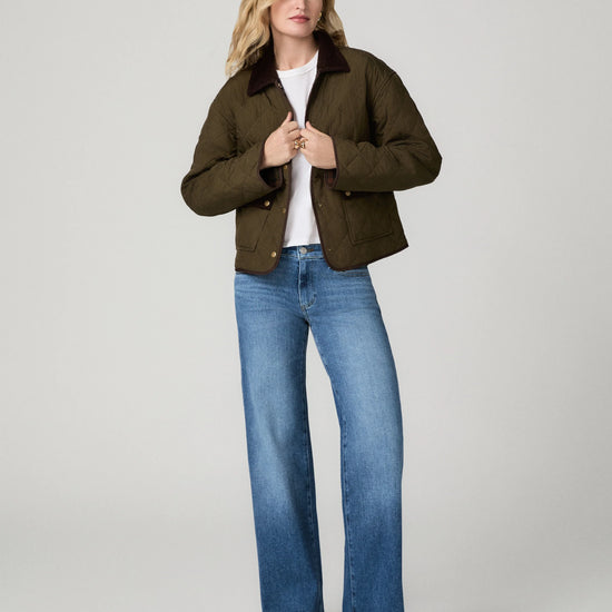 Model wearing blue jeans and a green coat on a grey background