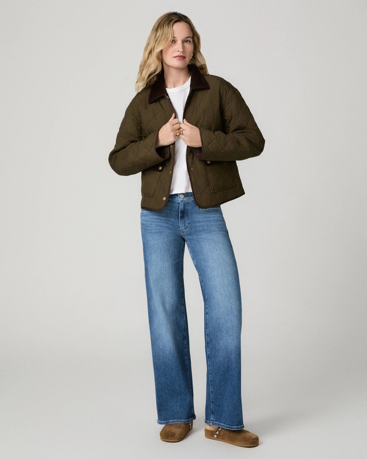 Model wearing blue jeans and a green coat on a grey background