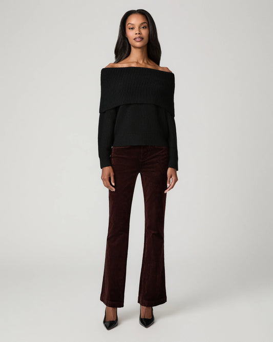 A model stands against a light gray studio background wearing a black off-the-shoulder long-sleeve top and dark burgundy velvet flare pants with black pointed heels.