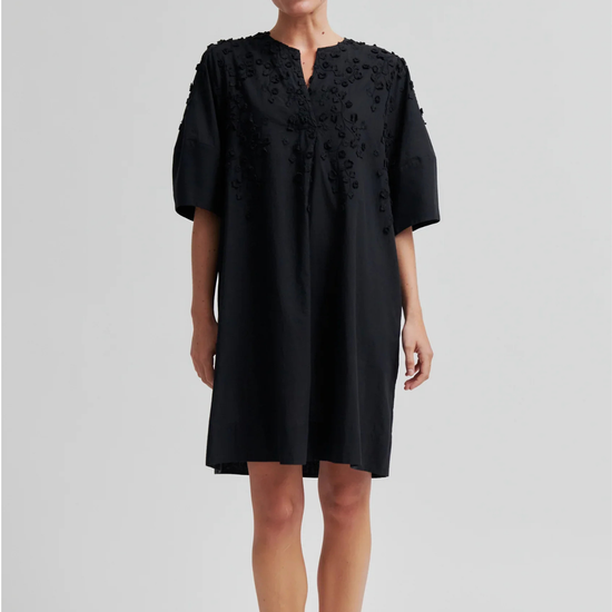 Woman wearing a black dress with intricate detailing on a light gray background