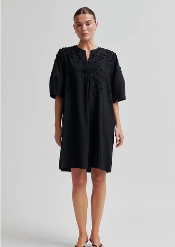 Woman wearing a black dress with intricate detailing on a light gray background