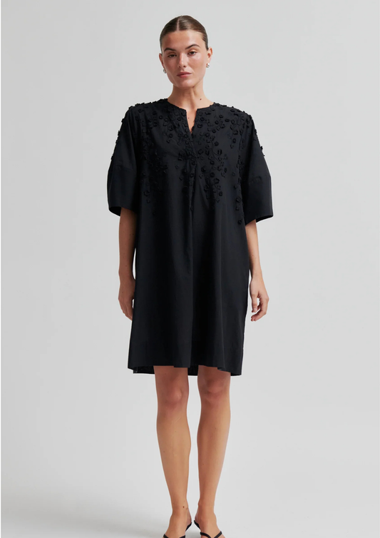 Woman wearing a black dress with intricate detailing on a light gray background