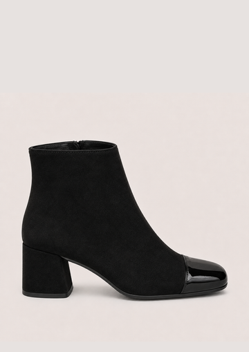 A black ankle boot with a matte suede-like body and a glossy patent leather toe cap, set against a plain light beige background.