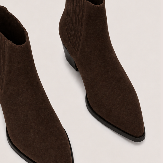 A pair of dark brown pointed-toe ankle boots with ribbed knit elastic sides, shown on a light beige background.