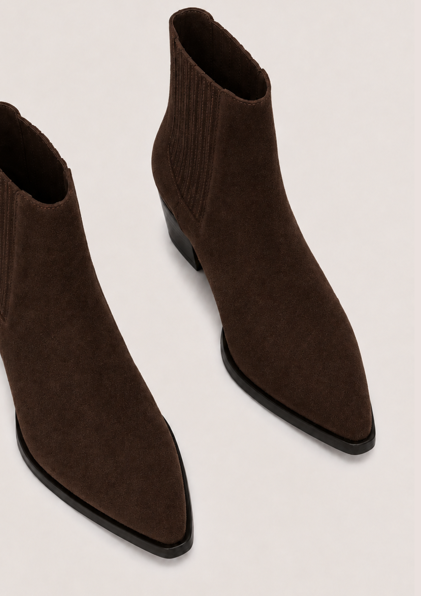 A pair of dark brown pointed-toe ankle boots with ribbed knit elastic sides, shown on a light beige background.