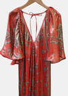 Red and gold patterned dress on a hanger against a white background
