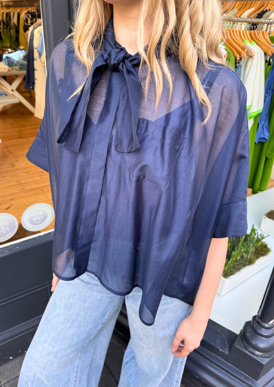 Person wearing a navy sheer blouse with a bow detail.
